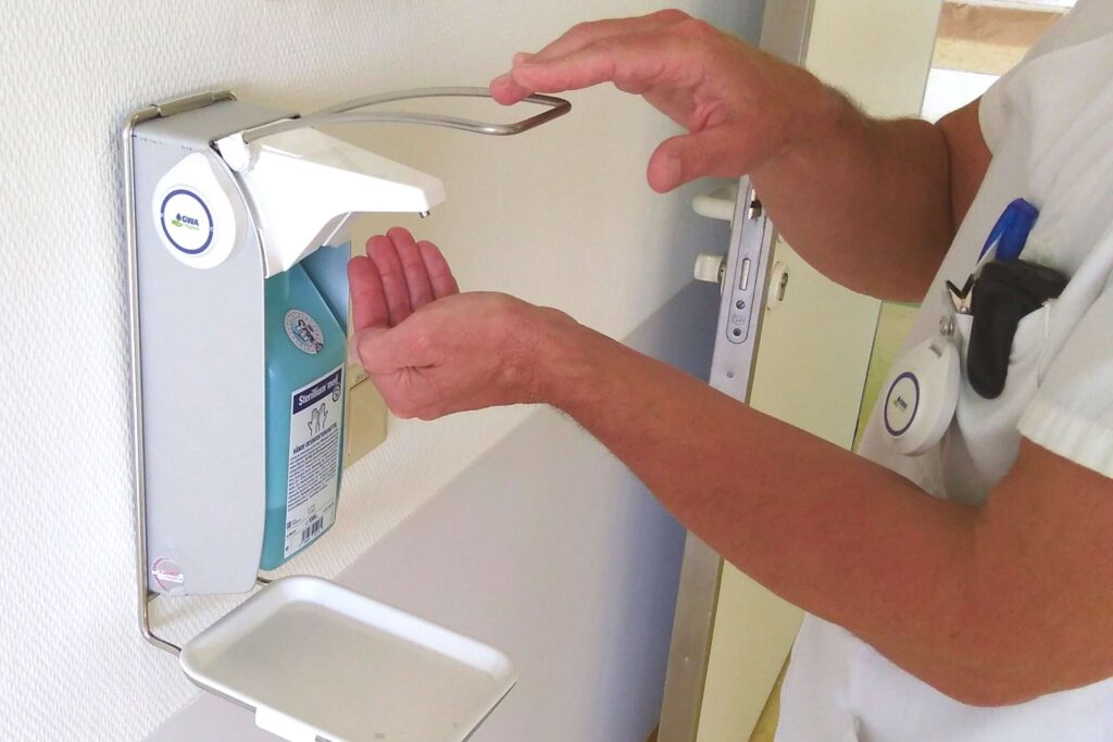 Medizinischer Mitarbeiter desinfiziert sich die Hände an einem Desinfektionsmittelspender mit GWA-Transponder